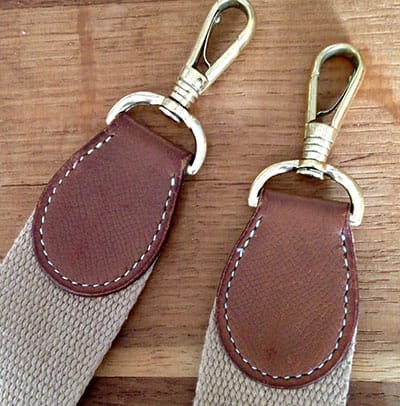 2 bouts de sangle de sac en bandoulières Hermès vintage. 2 attaches métal dorées fixées par un morceaux de cuir lui-même cousu à la main en point sellier sur une nouvelle sangle