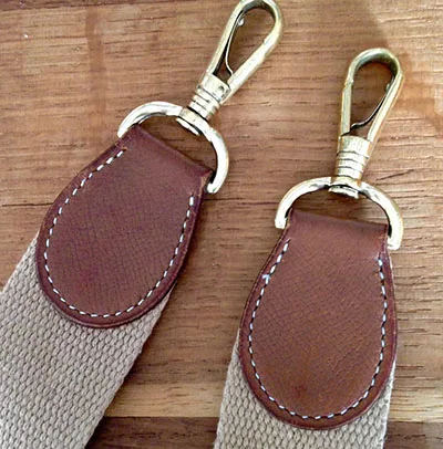 2 bouts de sangle de sac en bandoulières Hermès vintage. 2 attaches métal dorées fixées par un morceaux de cuir lui-même cousu à la main en point sellier sur une nouvelle sangle
