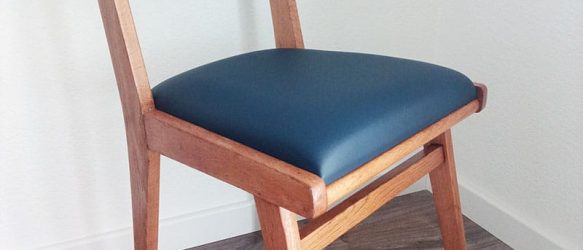 Chaise vintage pieds compas dans un bois de couleur moyenne. le dossier a été refait avec une toile coton/lin de mallorque en ikat rayé bleu/vert/écru. L'assise est en mousse ferme est recouverte d'un simili marin bleu marine.