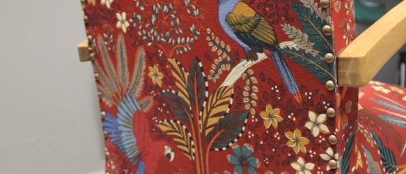 Dos d'un fauteuil bridge recouvert avec un tissu Thevenon fond brique et motif floral et animalier multicolore. Finition clous de tapissier espacés